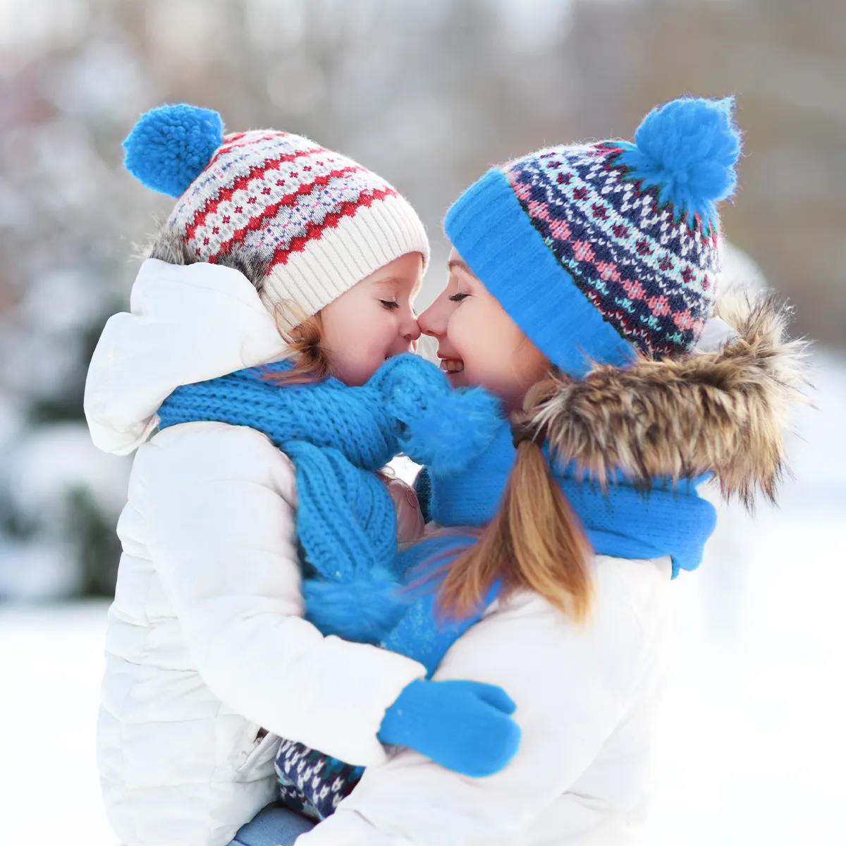 Mutter hält ihr Kleinkind im Winter draußen im Schnee, beide warm angezogen mit Mütze und Schal, Nähe und Geborgenheit als Schutz in der Erkältungszeit.